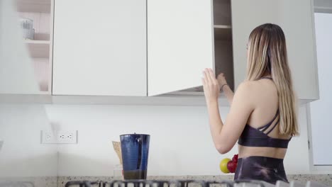 mujer caucásica bastante deportiva tomando un vaso del armario para verter jugo natural