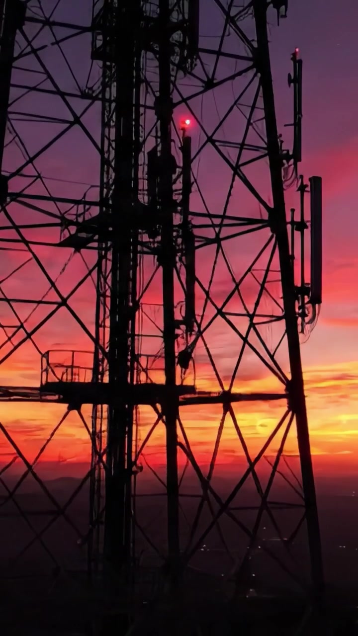 Uma Silhueta Deslumbrante de uma Torre de Comunicação ao Nascer do Sol Contra um Céu Vibrante, Exibindo Cores Marcantes do Amanhecer e da Transição da Noite