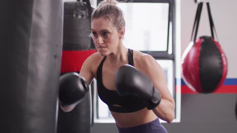 Video-Einer-Selbstbewussten,-Entschlossenen-Kaukasischen-Frau-In-Boxhandschuhen,-Die-In-Einem-Fitnessstudio-Mit-Einem-Boxsack-Trainiert