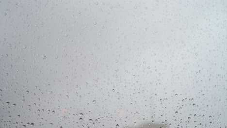 a close-up view of heavy rain drops is seen through a window glass