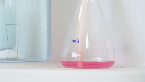 flask container with pink liquid making bubbles in a laboratory for chemical testing