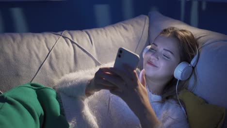 Cheerful-young-woman-lying-on-sofa-listening-to-music.