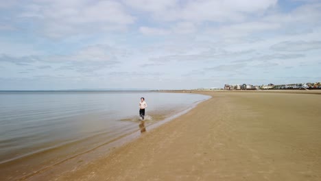barefooted man running in the water making splashes and wearing no shirt