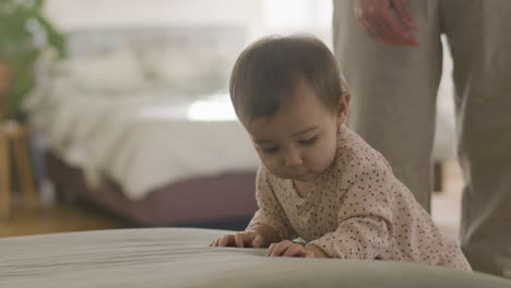 Adorable-Little-Baby-In-Pajamas-Walking-And-Taking-Her-First-Steps-Near-Sofa-While-Dad-Looking-After-Her