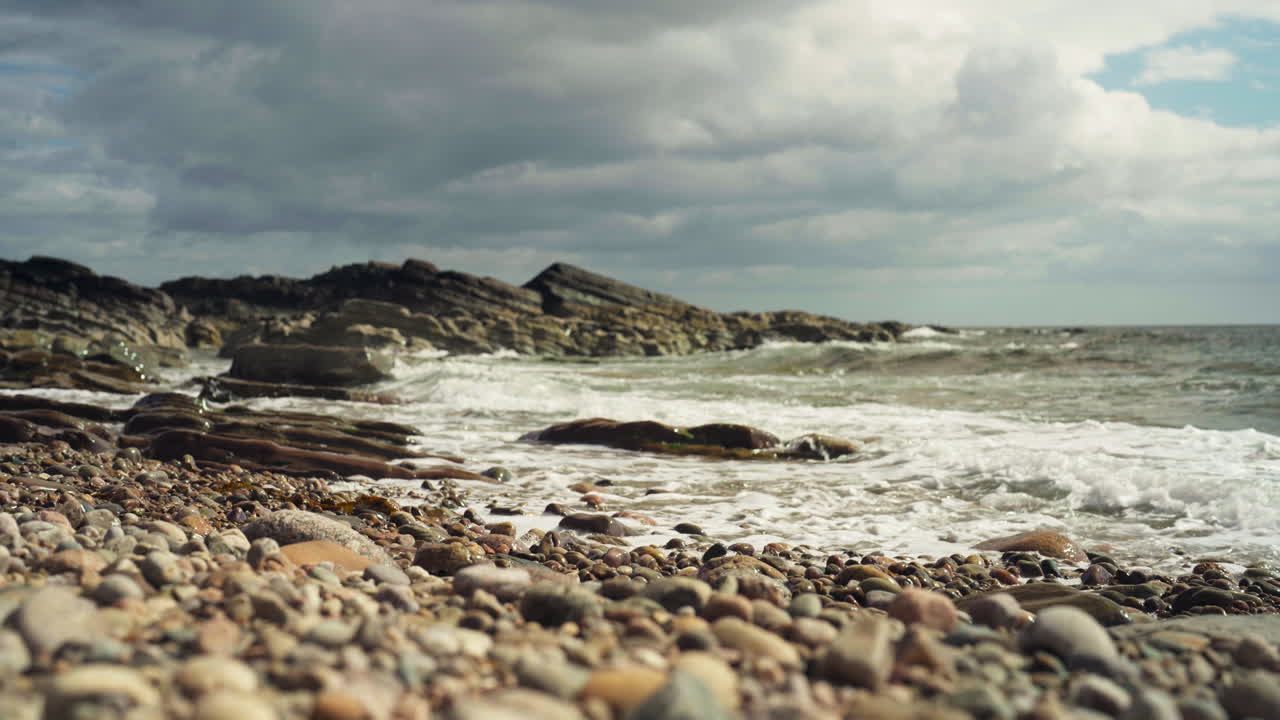 Static shot of sea water reaching a pebble beach in the day with cloudy sky, exterior