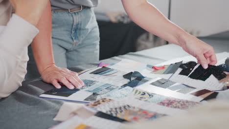 close view of designers carefully choosing fabric pieces attached to sample sheets during creative project planning session, focusing on texture, color, and quality in bright fashion design workspace