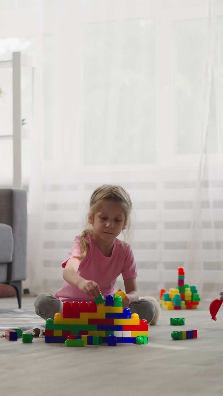 la niña construye una casa con bloques de plástico multicolores mientras el niño juega con juguetes. los hermanos se sientan en el suelo de la sala de estar disfrutando del fin de semana