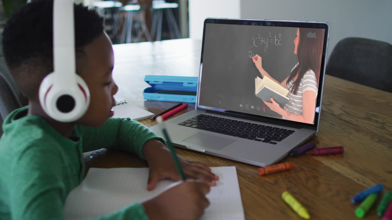 African american boy doing homework while having a video call with female teacher on laptop at home