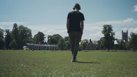 Young-caucasian-man-walking-on-the-green-grass-of-a-park-in-Cambridge,-England