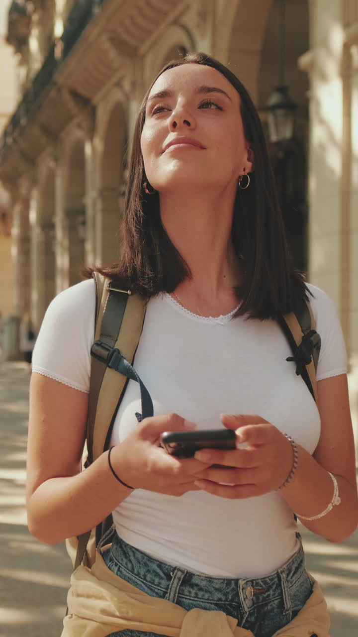 Giovane donna turista che si guarda intorno con lo smartphone in mano in città