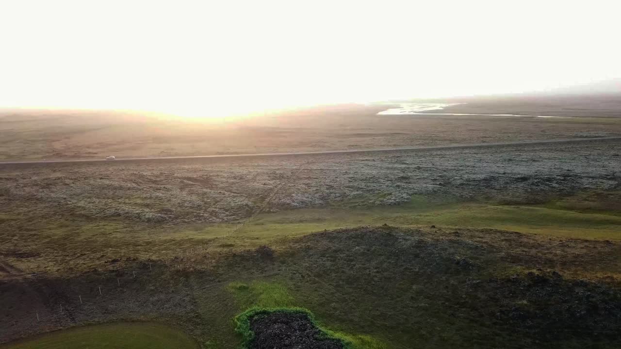 Golden sunset highlighting a quiet road cutting through Gönguleið um Eldhraun's rugged volcanic terrain, with green patches and vast lava fields defining Iceland's breathtaking natural beauty