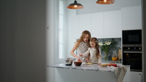 Involved-mom-and-child-kneading-dough-on-table.-Cute-family-preparing-pastry