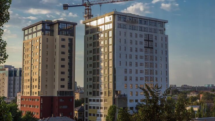 Guindaste e canteiro de obras contra o céu azul em timelapse aéreo. Trabalhadores pintando paredes de novo edifício residencial de apartamentos