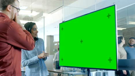 late at night male and female in conference room have discussion about mock-up chroma key green screen tv.