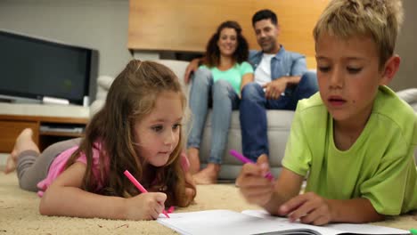 hermanos coloreando en el suelo mientras sus padres están sentados en el sofá