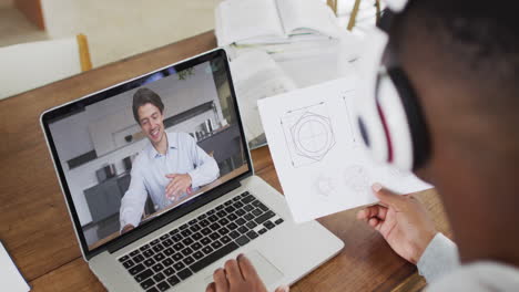 african american businessman sitting at desk using laptop having video call with male colleague