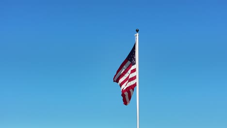 american flag on a pole waving flapping in the wind with no clouds and blue sky