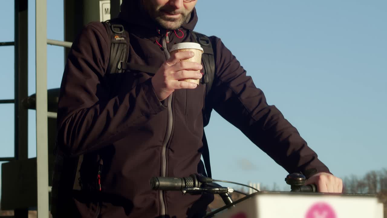 un joven en una bicicleta compartida disfruta de una taza de café en una mañana bañada por el sol