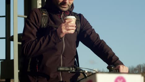 Un-Joven-En-Una-Bicicleta-Compartida-Disfruta-De-Una-Taza-De-Café-En-Una-Mañana-Bañada-Por-El-Sol