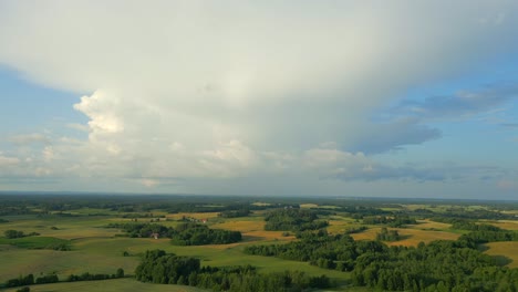 aerial view of a flat landscape with fertile fields over which huge clouds form