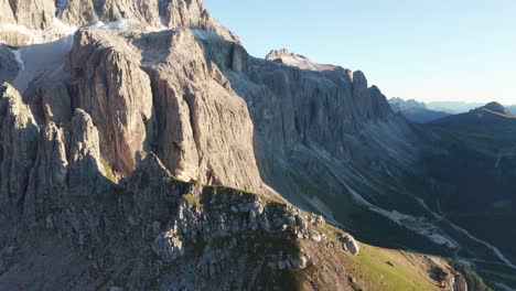 aerial forward flight along rocky sella pass mountains lit by the sun - dolomites mountain range with blue sky