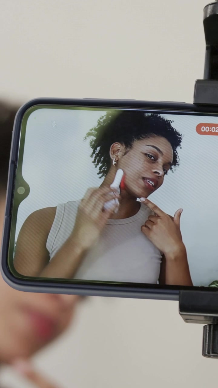 Vertical video: Phone timer starting woman in tan top gliding device on jaw at vanity, for demo