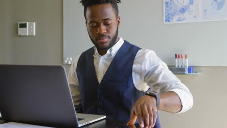 Vorderansicht-Eines-Jungen-Schwarzen-Geschäftsmannes,-Der-Mit-Laptop-Sitzt-Und-Im-Büro-Mit-Dem-Mobiltelefon-Telefoniert-4k