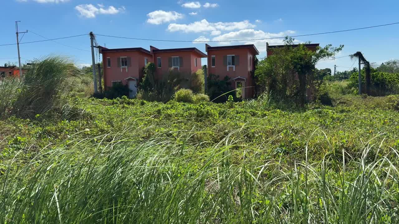 Bakkenivåperspektiv som viser parallelle forlatte hus med tykt vilt gress som dominerer området.