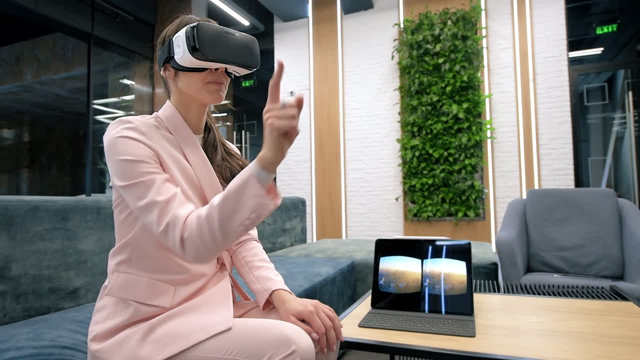 A blonde caucasian woman exploring virtual reality using VR glasses in an office. Tablet on the table showing image visible in the headset