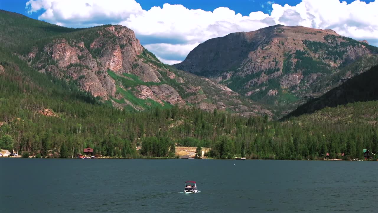 Grand Lake Granby pontoon boating sailboat spring summer aerial drone Colorado Rocky Mountains National Park entrance sunny morning daytime clouds lake homes blue sky sunny clouds parallax follow