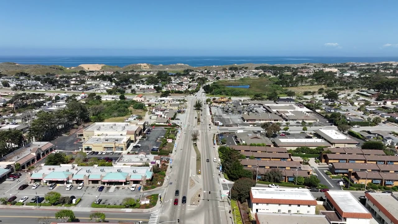Kinoreife Drohnen-Luftaufnahme von Marina, Kalifornien, die Wohnviertel, kommerzielle Einkaufsviertel, belebte Stadtstraßen, malerische Küstendünen mit der Monterey Bay und dem Pazifischen Ozean zeigt.