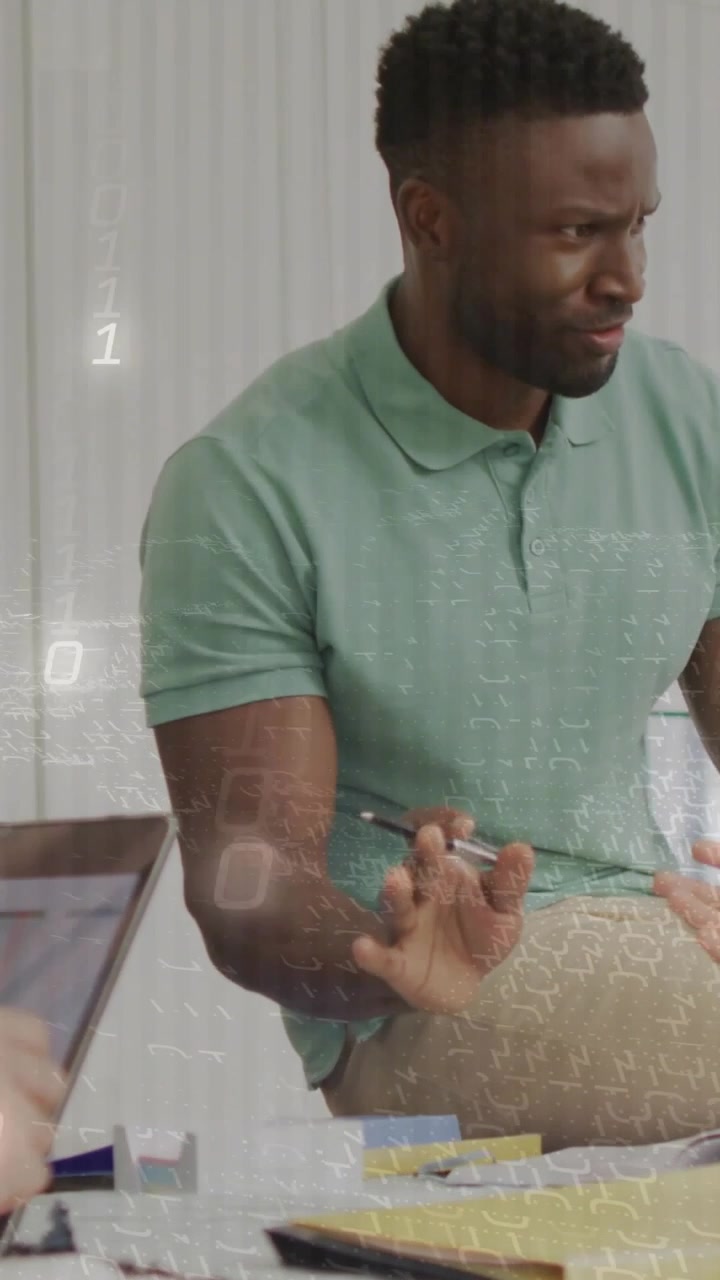 Vertical video: Man in polo answering coworker in office meeting, gesturing pen by laptop