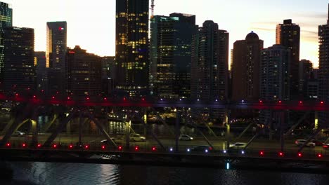 Paisaje-Urbano-Iluminado-En-El-Centro,-Puente-De-Historia-Histórico-Catalogado-Como-Hertiage-Con-Tráfico-Intenso-Que-Cruza-El-Río-Al-Atardecer,-Ciudad-De-Brisbane,-Queensland,-Tiro-De-Seguimiento-Cinematográfico