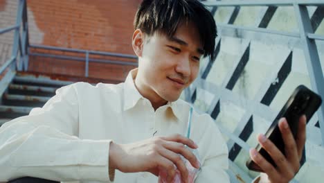 young man drinking smoothie and using phone outdoors