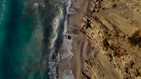 Vista-De-Arriba-Hacia-Abajo-De-Las-Olas-Del-Mar-Salpicando-Y-Espumando-En-La-Ladera-Rocosa-Del-Mar-Jónico,-Textura-Del-Agua