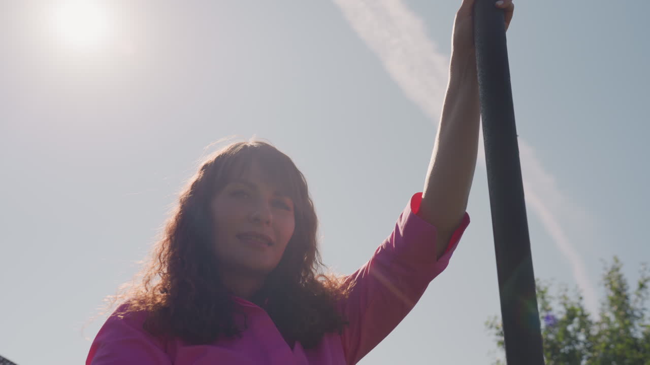 Caregiver Adjusts Safety Net Properly, Sunlit Scene Of Woman Securing Garden Trampoline Safety, Responsible Individual Ensures Trampoline Safety By Securing Pole In Sunny Garden Environment