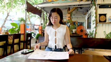 asian girl checking food menu at vietnamese restaurant. medium shot