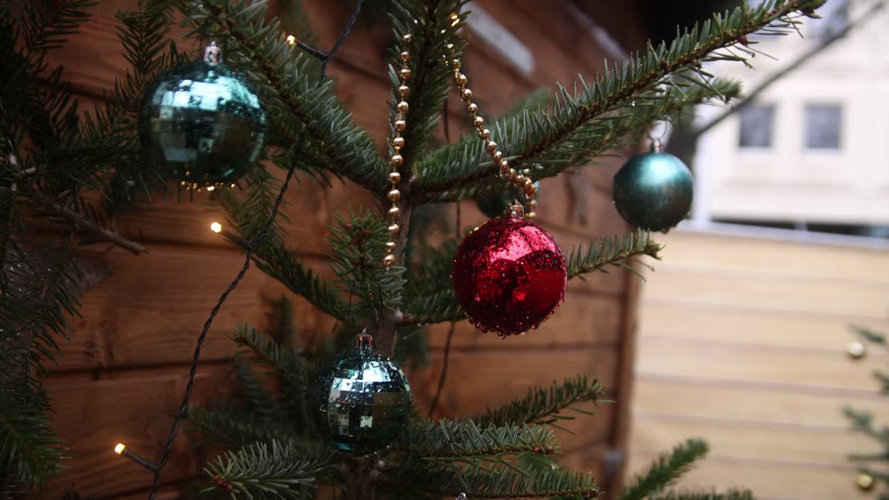 adornos de navidad rojos y verdes colgados en un árbol frente a un chalet de madera en heidelberg, alemania en un mercado navideño festivo en europa
