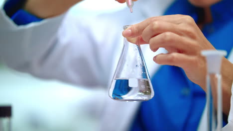 woman chemist adding chemical reagent in pure liquid at glass flask