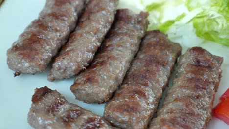 cerca de pinzas de kebab a la parrilla en un plato con lechuga, tomate y cebolla