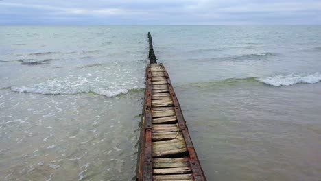 establishing aerial view of baltic sea coast on a overcast day, old wooden pier, white sand beach, low waves crushing against the coast, climate changes, wide drone shot moving forward slow