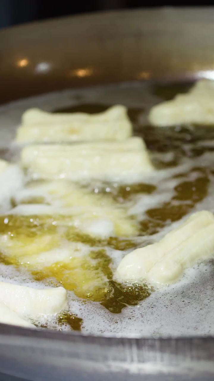Close-up of traditional Chinese dough sticks frying in bubbling hot oil within a large wok.