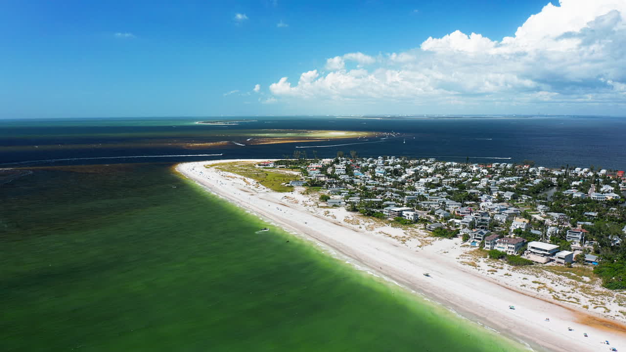 A coastal peninsula community lies between emerald shallows and offshore sandbars, where sandy beaches connect residential living with the wide expanse of open sea
