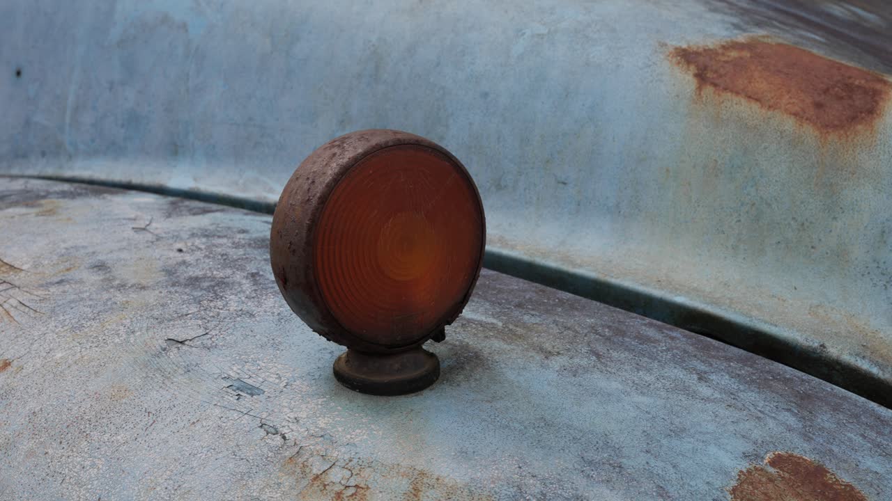 Close up of a weathered orange light on a faded and scratched blue truck hood