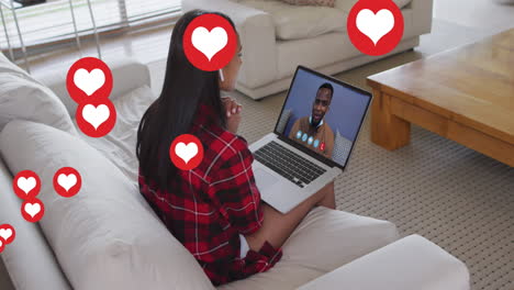 animation of social media heart icons over woman using laptop of video call in background