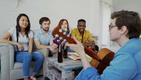 jóvenes amigos felices tienen una fiesta tocando la guitarra y cantando juntos en casa