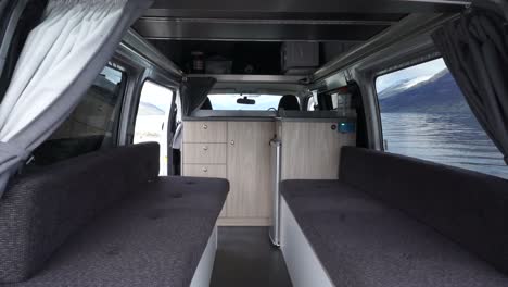 Exterior-and-interior-of-motorhome-by-beautiful-blue-Lake-Wakatipu,-Queenstown,-New-Zealand-with-mountains-fresh-snow-cloudy-sky-in-background