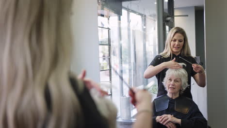 reflection in mirror of senior woman having hair cut by female stylist in hairdressing salon