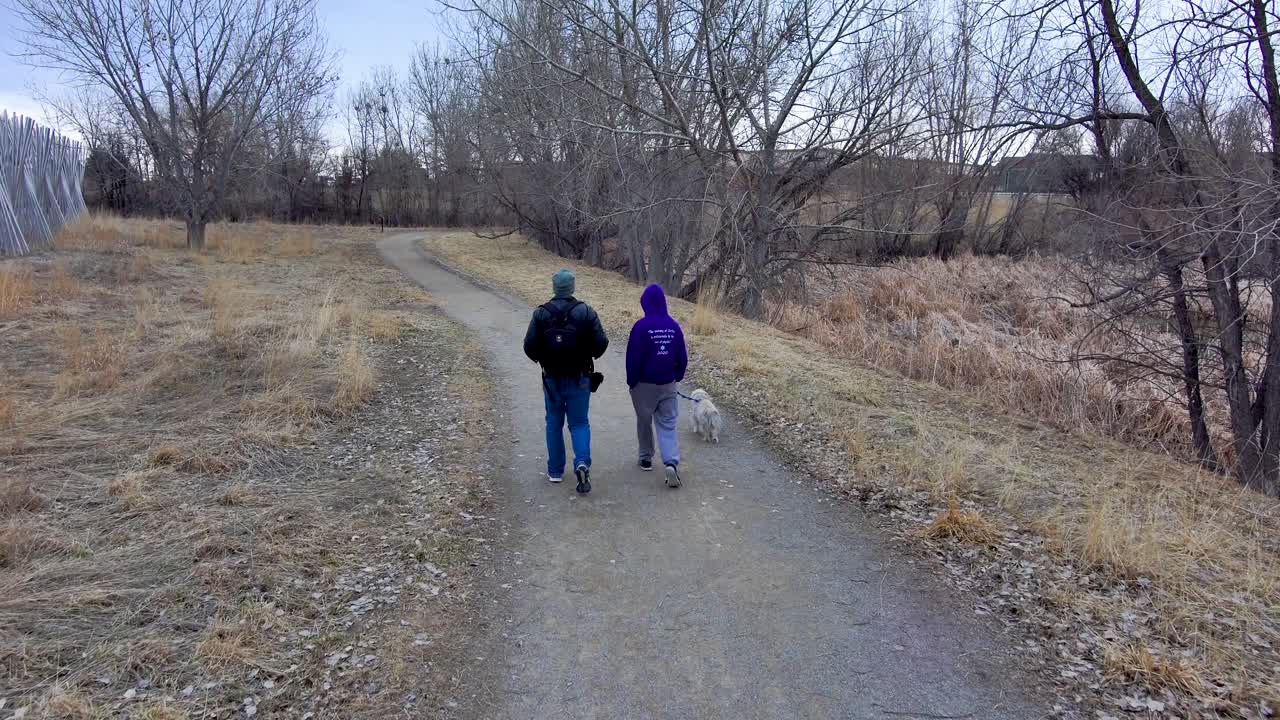 A father and his son  walk a dog on a gloomy winter trail.