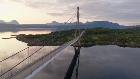 Drone-Asciende-Al-Puente-De-Narvik,-El-Cielo-Del-Atardecer-De-La-Hora-Dorada-Se-Refleja-En-Aguas-Tranquilas